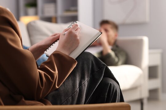 Professional psychologist making notes during therapy session with patient indoors, selective focus