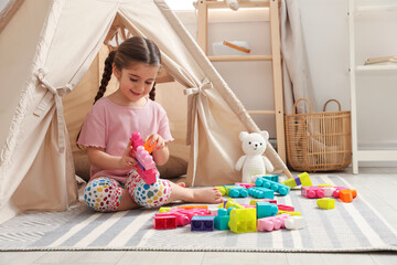 Little girl playing with building blocks near toy wigwam in playroom © New Africa