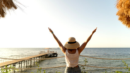 Woman stands by sea, arms raised in joy © I