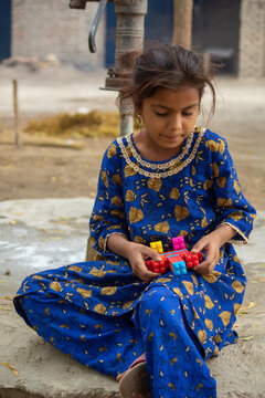 Little girl playing with toy while sitting on ground in rural village simple childhood lifestyle scene