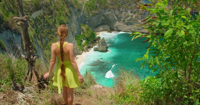 Woman walking on mountain edge watching tropical sea at Nusa Penida Bali Island