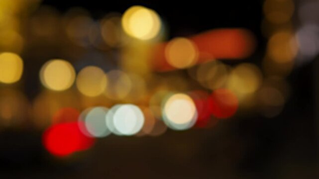 Static long exposure of city street at night with bokeh effect. Light sources from streetlights and vehicle traffic appear as soft out of focus circular orbs. Warm yellow, white, red, green colors