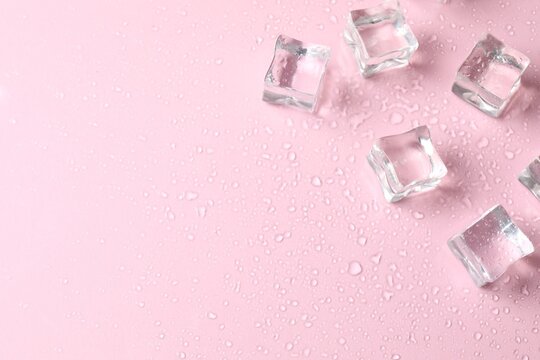 Ice cubes with water drops scattered on pink background, top view.