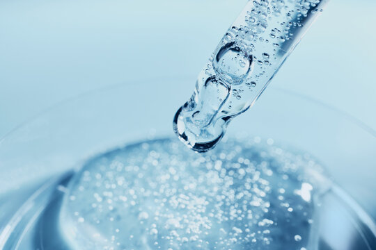 Glass dropper applying liquid with bubbles to petri dish in medical lab setting