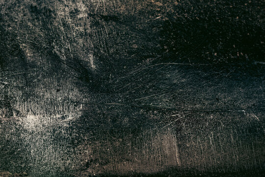 Dark, textured surface features numerous fine scratches and scuffs creating an aged appearance.