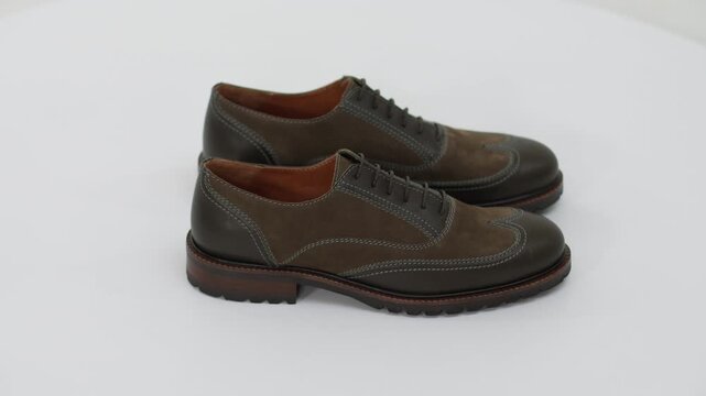 Pair of classic brown suede and leather men's brogue shoes rotating on a white background, displaying elegant footwear fashion