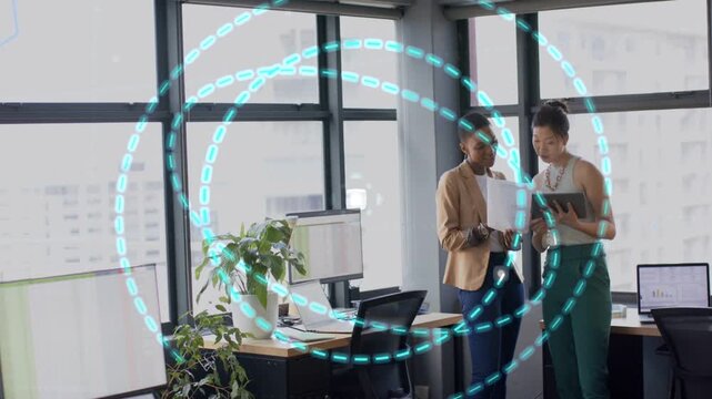 Two businesswomen reviewing doc with paper and tablet as teal rings arising expanding overlapping