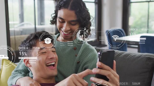 Man reclining and nonbinary partner leaning on couch tapping phone, sharing AR finance HUD icons