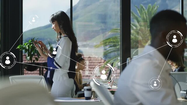Standing woman tapping smartphone, creating node overlay linking team laptops and desks