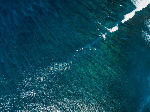 Drone shot of surfers riding waves over coral reef in Bali, tropical surf trip