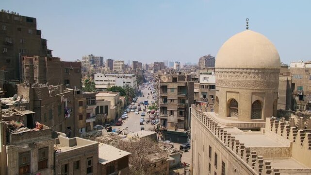 Dense urban district in Cairo featuring prominent mosque dome in foreground and busy street stretching through tightly packed buildings. Dome of Madrasa of Sarghatmish, Islamic Cairo, Egypt