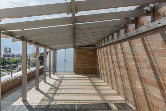 A large terrace is seen with a wooden beam structure and an open view of the sky. Sunlight creates shadows on the floor, and the area is empty and ready for use