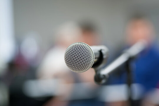 Selective focus on a condenser microphone in front of an unrecognizable crowd. Professional setup for a seminar, lecture, or corporate presentation from the stage. Photo