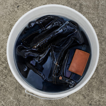 raw denim selvedge jeans getting soaked in bleach inside of a blue plastic bucket top view