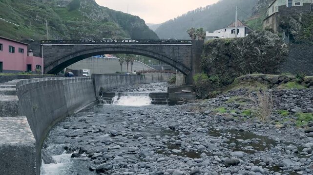 Mountain river flowing under a stone arch bridge in madeira
