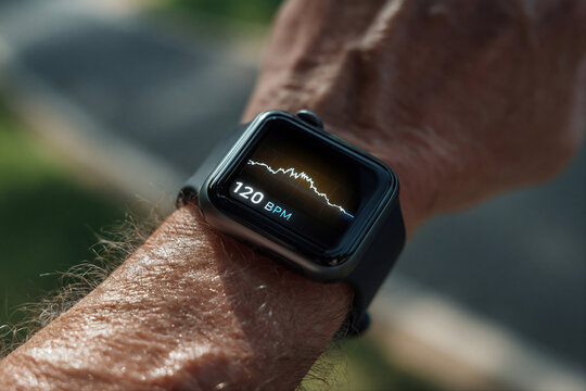 Hand of elderly man with heart monitor on his wrist against the background of blurred treadmill. Fitness tracker, pulsometer and healthy aging concept. Macro shot for poster, product promotion 