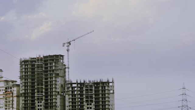 Timelapse Tower crane above unfinished high-rise buildings in Delhi under cloudy sky, representing urban growth, real estate development and construction industry progress.