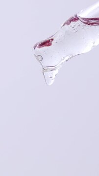 Cosmetics transparent liquid gel dripping from glass pipette on white background, vertical video format