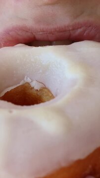 Caucasian woman eating donut with white sugar icing close up, vertical video