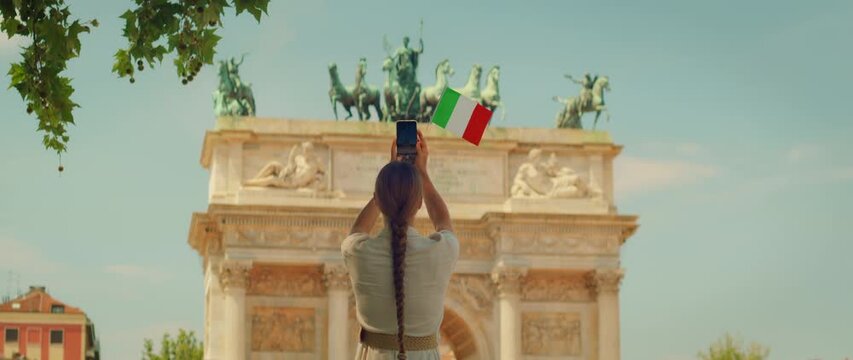 Woman photographing Arco della Pace in Milan with Italian flag in hands, Italy