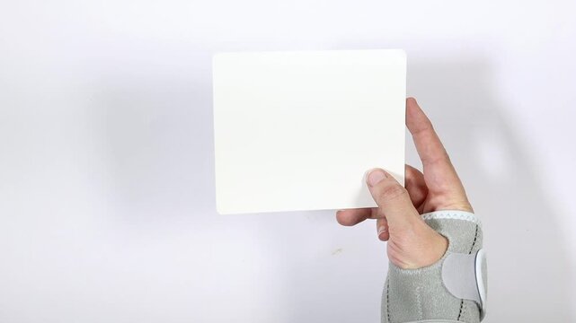 Hand Wearing Wrist Brace Holding Blank White Card On Clean White Background For Mockup