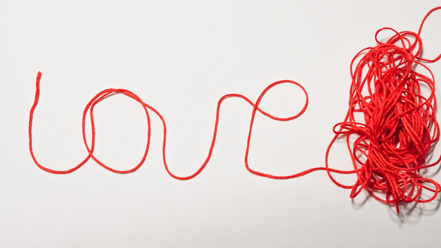 Red string forming the word love with tangled yarn on white background