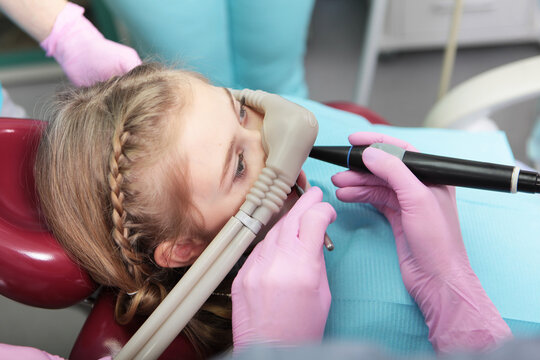 Little girl is comfortable to treat her teeth under superficial sedation. Girl smiles and holds two thumbs up. Treatment of children's teeth with nitrous oxide. Milk teeth treatment.