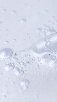 Cosmetics transparent liquid gel taking with glass pipette on white background, vertical video format