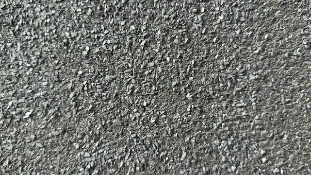 Close-up rolled roofing granules texture, coarse mineral surface on bitumen membrane, grey aggregate fragments, protective coating.