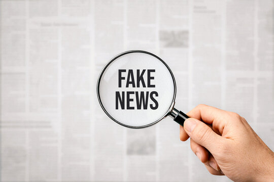 Magnifying glass highlighting fake news text over newspaper background. Media misinformation, fact checking and disinformation concept
