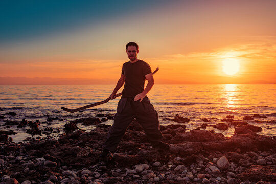 Man with wooden stick on rocky shore at vivid sunset