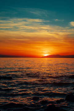 Colorful sunset over calm Issyk-kul lake with mountain silhouette horizon, Kyrgyzstan