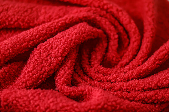 Red teddy fleece fabric with curly swirls and selective focus on soft textile texture.Detailed view of bright red teddy bear fabric draped in elegant soft folds. Vibrant curly fleece material 