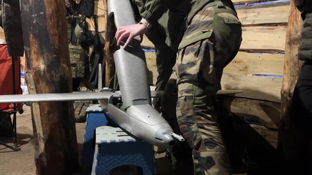 Serviceman in a dugout preparing an aircraft-type attack drone before launch. Concept of modern warfare, unmanned aerial systems, and drone operations during active hostilities. Military technology