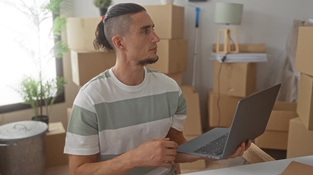 Man holding laptop and pointing finger amid stacked moving boxes in a building living room of a new home; focused planning.