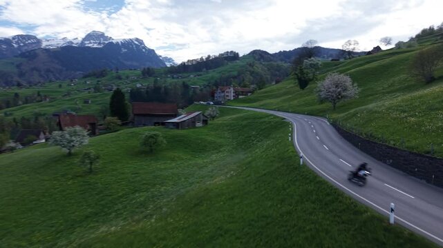 Low altitude drone shot moving backward as a motorcycle approaches, creating a dynamic perspective of motion on a mountain road.