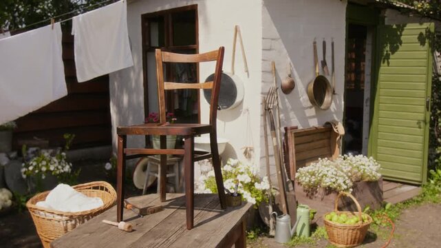 Full no people shot of freshly painted vintage wooden chair standing on work table in yard of country home, drying in fresh air after restoration and repair, white cottage and flowers in background