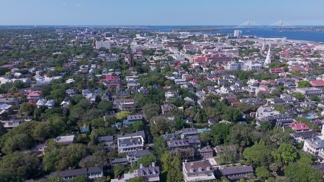 Aerial - Flying over the residential area at the south end of the Charleston, SC peninsula toward the historic town center with harbor and Cooper River Bridge in the distance