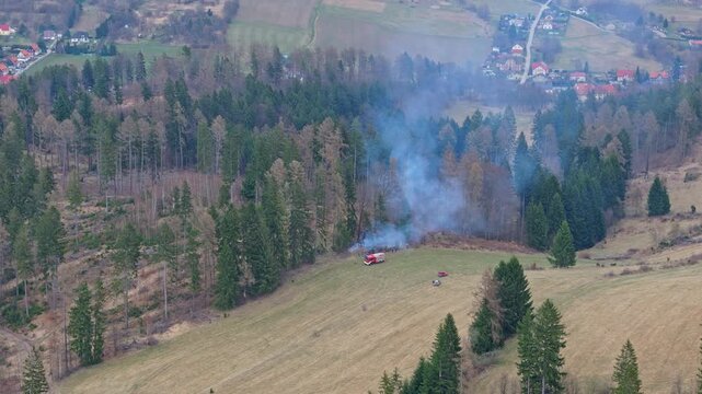 Fire incident in forest with emergency response vehicles and firefighting action near hunting stand captured from above