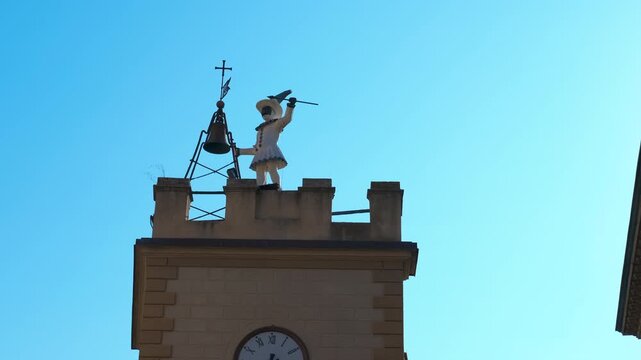 Harlequin automaton hitting the bell on a clock tower. Iconic automaton of harlequin, or arlecchino, dressed in a traditional costume and striking a bell with a mace on top of a clock tower