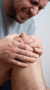 Man writhing in severe knee pain holding leg in distress, acute pain concept, vertical video close up.