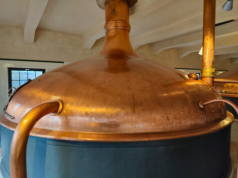 Close-up of a large copper brewing kettle in a traditional craft brewery. Polished copper surface, industrial brewery setting, historic brewing process.