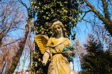 Fototapeta premium Sad angel statue in autumn light with golden wings, symbol of grief, loss, mourning and remembrance in peaceful cemetery atmosphere
