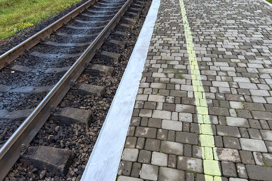 Train tracks and walkway border at a railway station in the countryside during a clear day