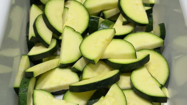 Chopped zucchini slices in container, fresh green squash for cooking close up, slow mode