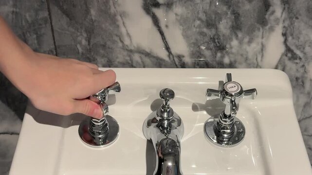 Hand pulling up sink stopper control on bathroom faucet, close up