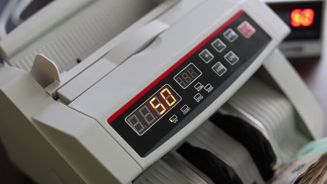 Closeup shot of banknote counting machine with Vietnamese Dong money (VND). Automatic currency counter equipment processing paper bill with Ho Chi Minh portrait vignette. Finance industry in Vietnam.