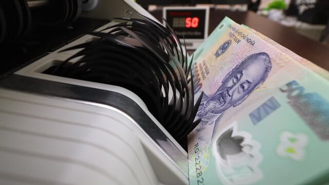 Closeup shot of banknote counting machine with Vietnamese Dong money (VND). Automatic currency counter equipment processing paper bill with Ho Chi Minh portrait vignette. Finance industry in Vietnam.