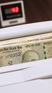 Closeup shot of banknote counting machine with Indian rupee (INR) money. Automatic currency counter equipment processing 500 rupees with Mahatma Gandhi portrait. Finance and banking industry in India.