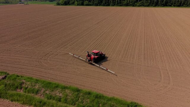 Tractor Spraying Farmland: Red tractor spraying fertilizer across a vast farmland field, rows neatly tilled in preparation for planting, seen from above.